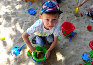 Chłopiec wsypuje piasek do wiaderka